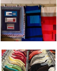 a variety of quilts are displayed on racks