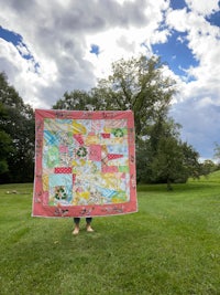 a woman holding up a quilt in a field